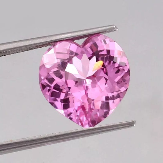 Heart-shaped Pink Morganite gemstone held by tweezers on a light gray background