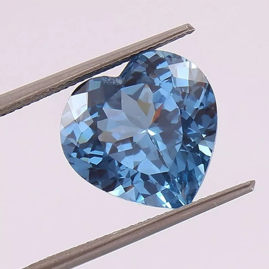 Aquamarine Blue gemstone held between tweezers against a light pink background
