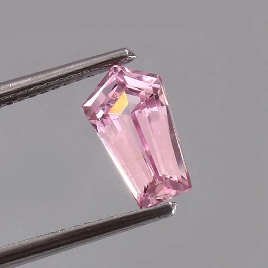 Pink Padparadscha Sapphire gemstone held by tweezers against a gray background