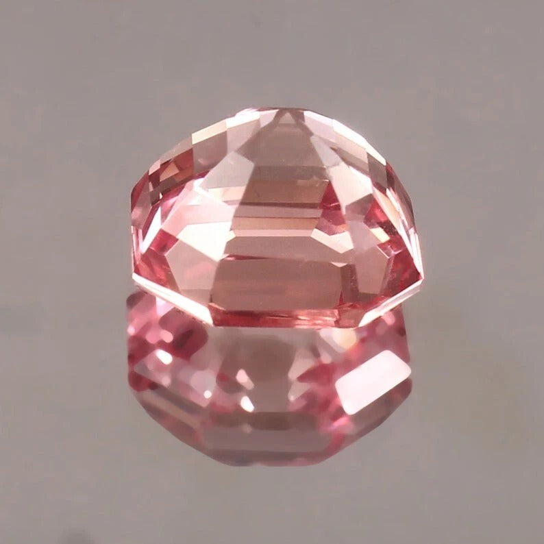 Padparadscha Sapphire on a reflective surface with a gray background