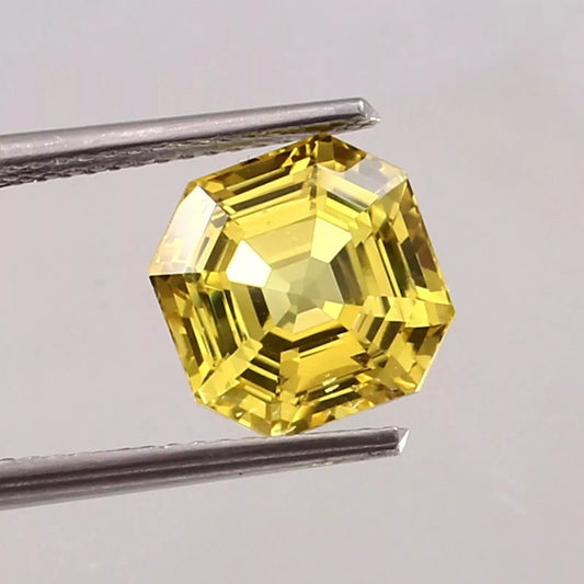 Yellow Sapphire gemstone held by tweezers against a gray background