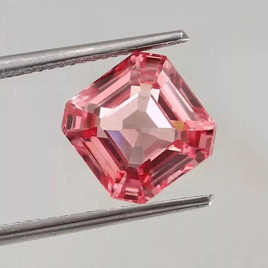 Padparadscha Sapphire gemstone held by tweezers on a light gray background