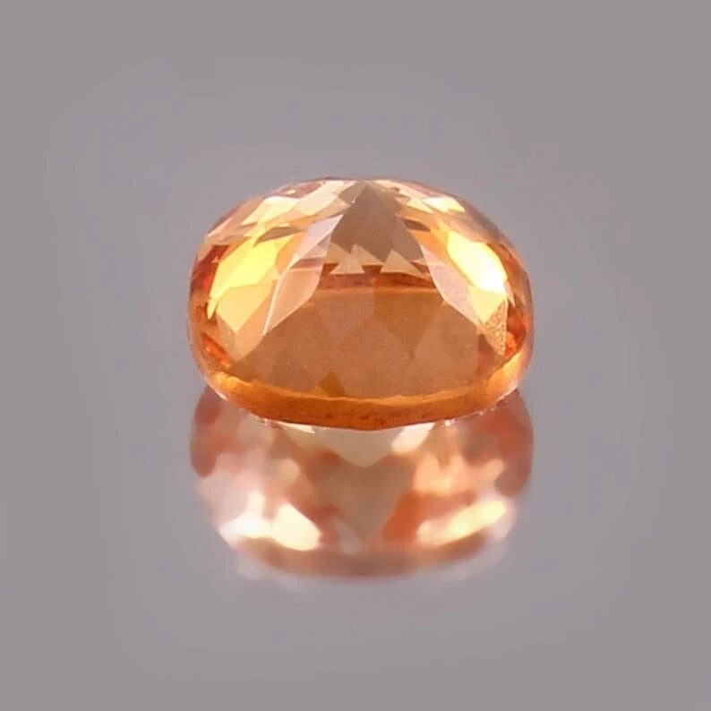 Faceted Padparadscha Sapphire – Peach to Orange gemstone on a reflective gray surface