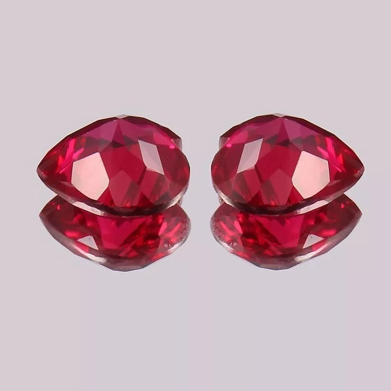 Pair Blood Red Mozambique Ruby gemstones on a reflective gray surface