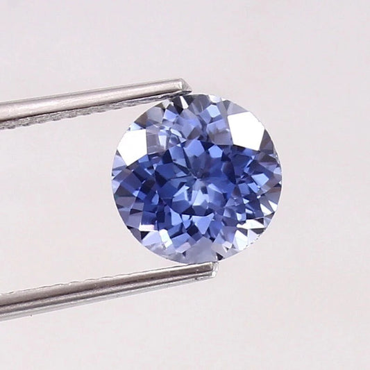Paste Blue Color Sapphire gemstone held by tweezers on a light gray background