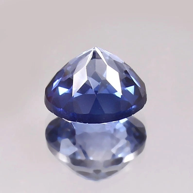 Faceted Paste Blue Color Sapphire gemstone on a reflective surface with a light gray background