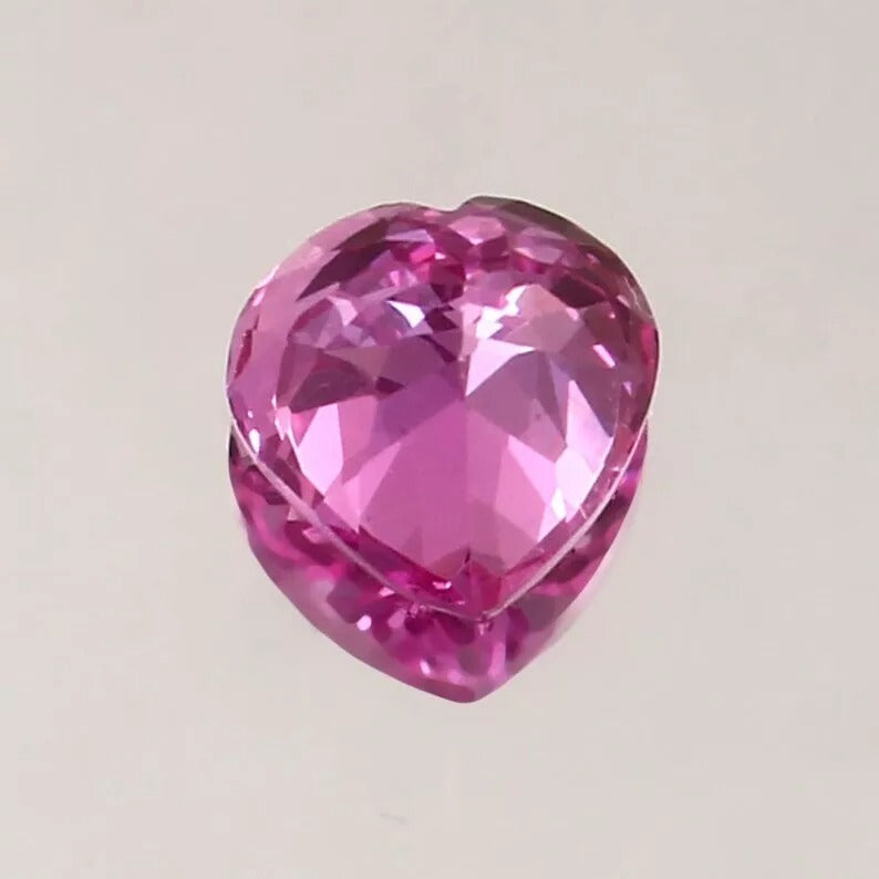 Heart-shaped pink sapphire gemstone on a light gray background