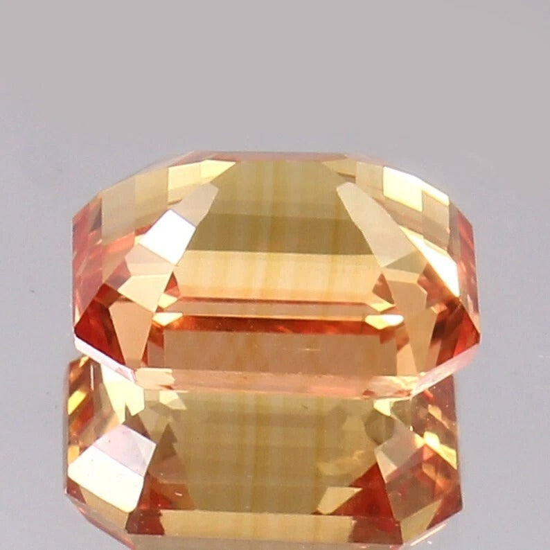 Faceted Peach Padparadscha gemstone on a gray background