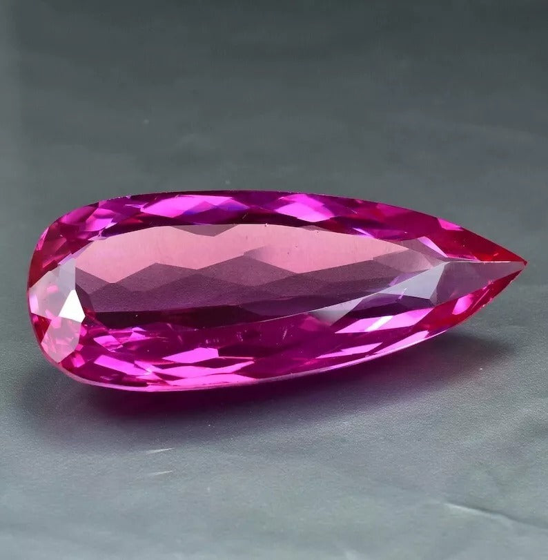 Faceted Royal Pink Ceylon Sapphire gemstone on a gray background
