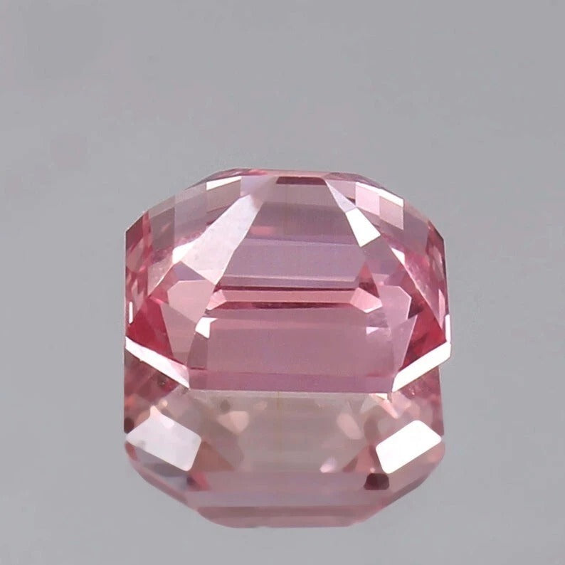 Faceted pink Padparadscha Sapphire gemstone on a gray background