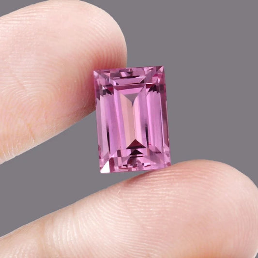 Pink Baguette Cut sapphire gemstone held between two fingers against a gray background