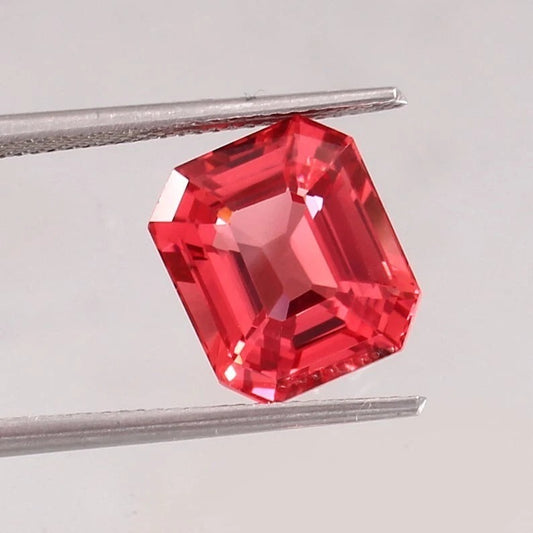 Padparadscha Sapphire gemstone held between tweezers on a light gray background