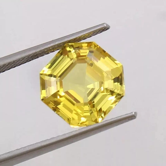 Sapphire asscher yellow gemstone held by tweezers against a light gray background