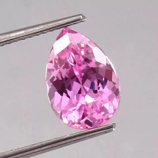 Pink Sapphire gemstone held by tweezers on a light gray background