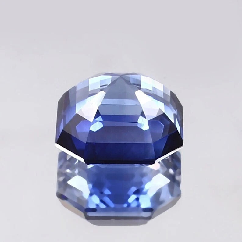 Faceted Cornflower Blue Sapphire gemstone on a light gray background