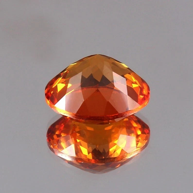 Faceted Orange Sapphire gemstone on a reflective gray surface