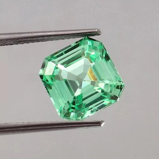 sapphire asscher cut green gemstone held by tweezers on a gray background