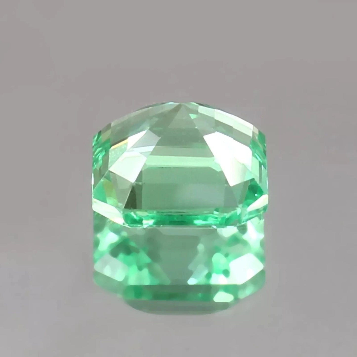 Faceted green sapphire asscher cut gemstone on a gray background