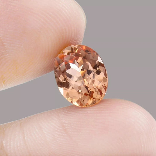 Peach Padparadscha Sapphire gemstone held between two fingers against a neutral background