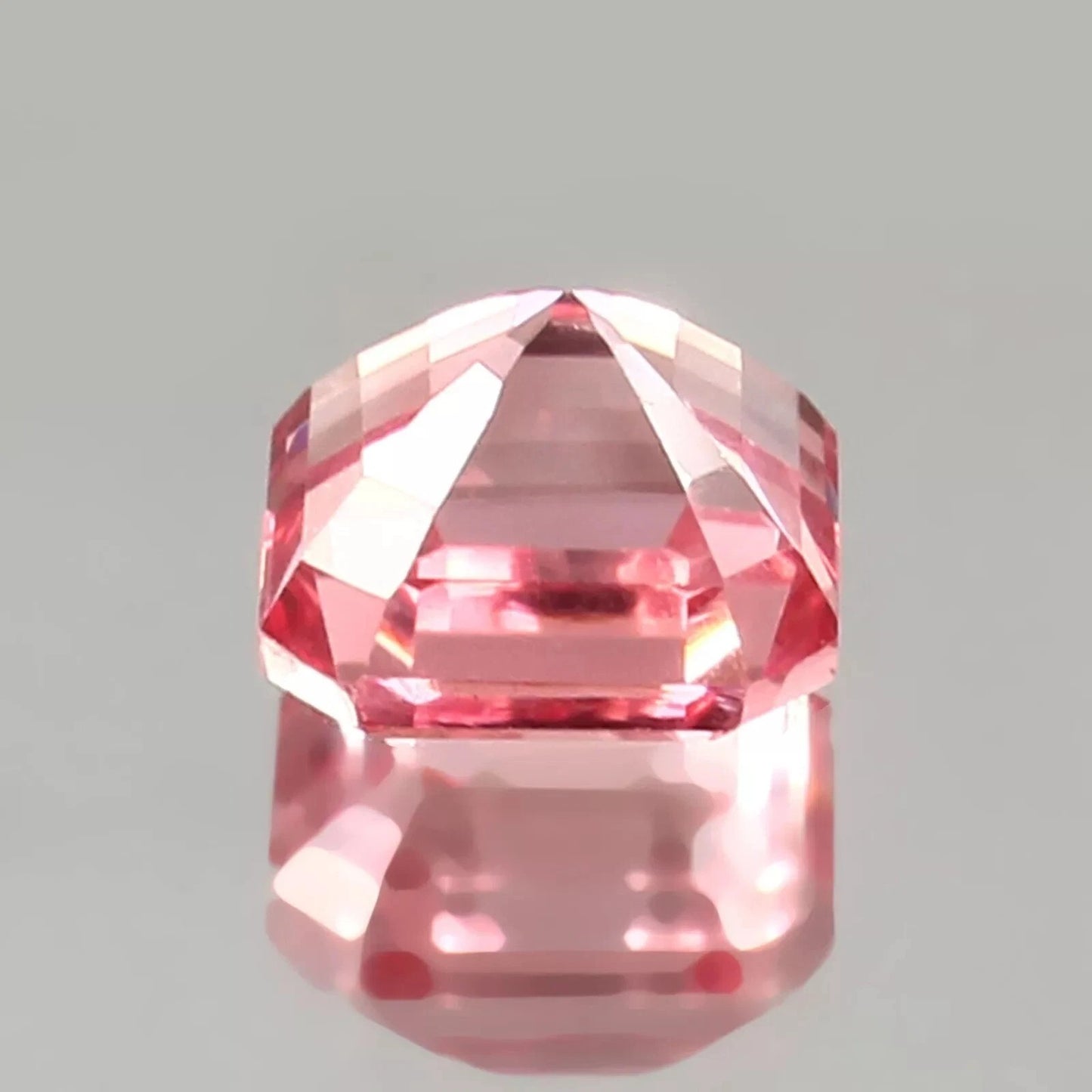 Faceted Natural Padparadscha Sapphire gemstone on a gray background