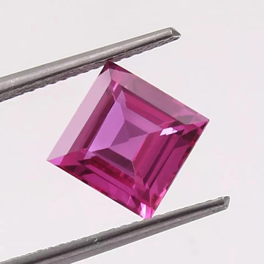 Square-cut Ceylon Pink Sapphire gemstone held between tweezers on a light gray background