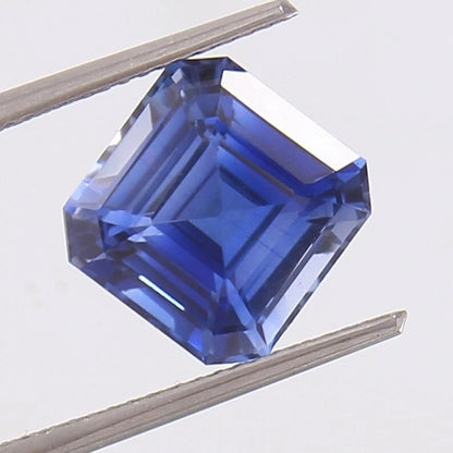 Royal Blue Sapphire held between two tweezers on a white background