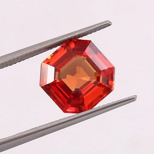 Red octagonal orange sapphire held between tweezers on a light pink background