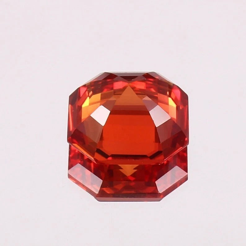 Faceted orange sapphire gemstone on a light gray background