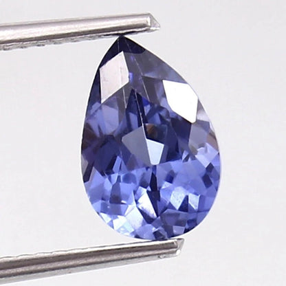 Teardrop-shaped blue Kashmir Sapphire gemstone held by tweezers on a white background