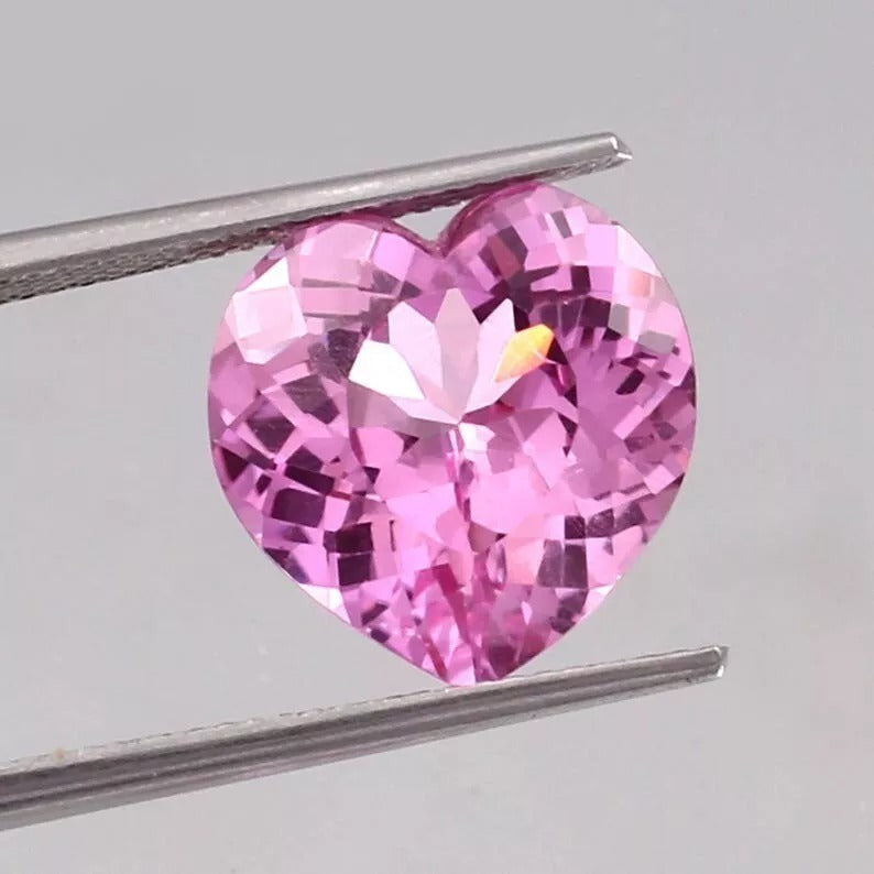 Heart-shaped Pink Morganite gemstone held by tweezers on a light gray background
