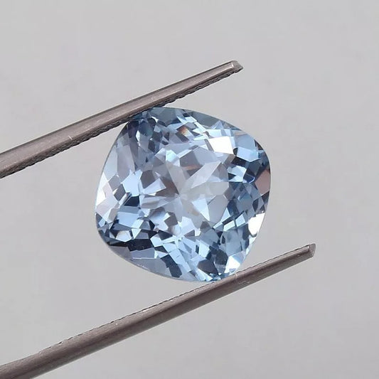 Blue Aquamarine gemstone held between tweezers against a neutral background