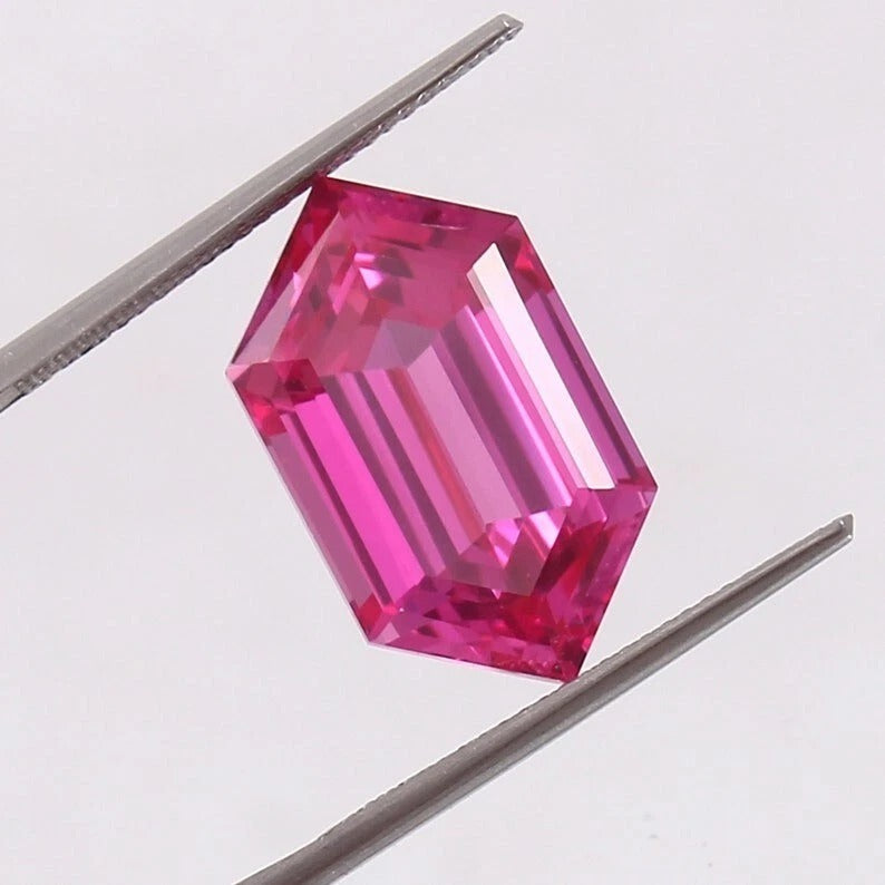Ceylon Pink Sapphire gemstone held between tweezers on a light gray background