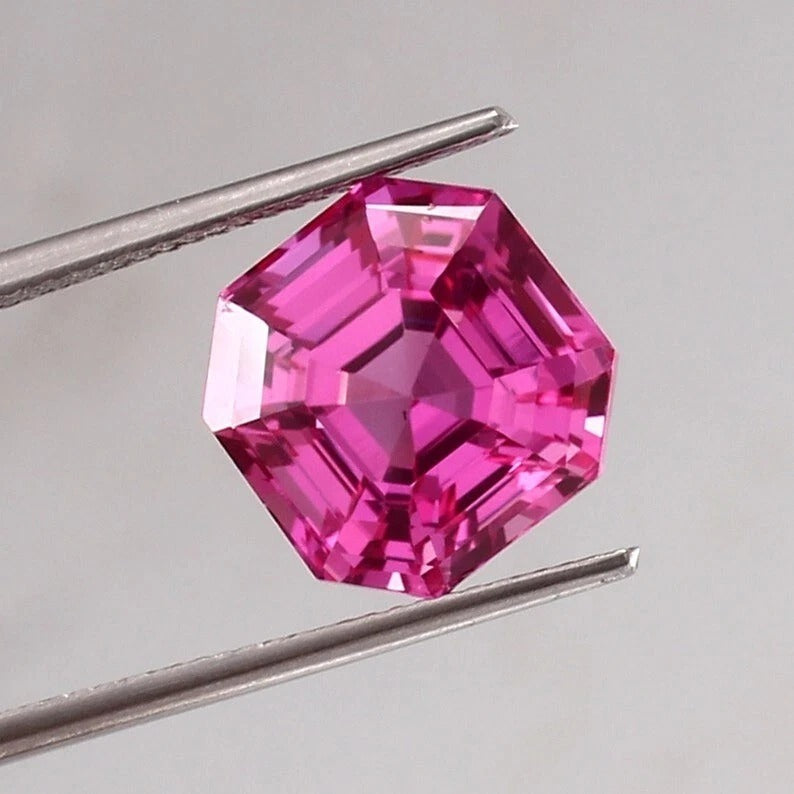  sapphire asscher pink gemstone held by tweezers against a gray background