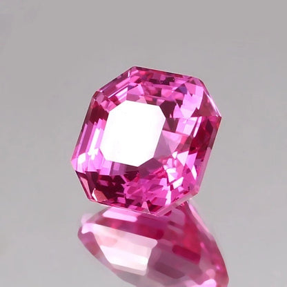 Faceted pink  sapphire asscher gemstone on a reflective gray surface