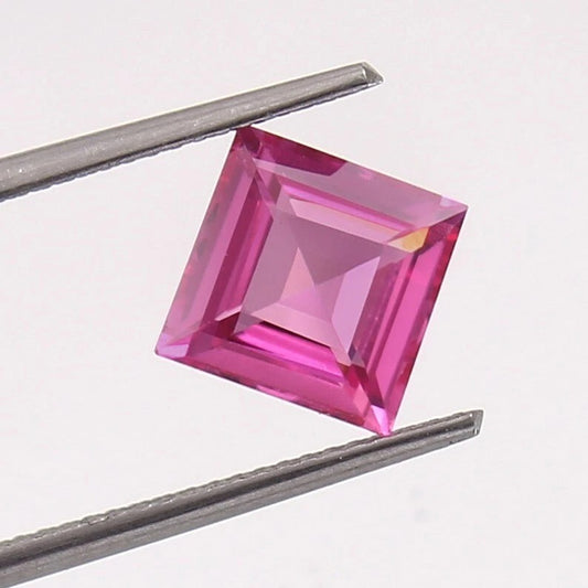 Square-cut pink Sapphire gemstone held between tweezers on a white background