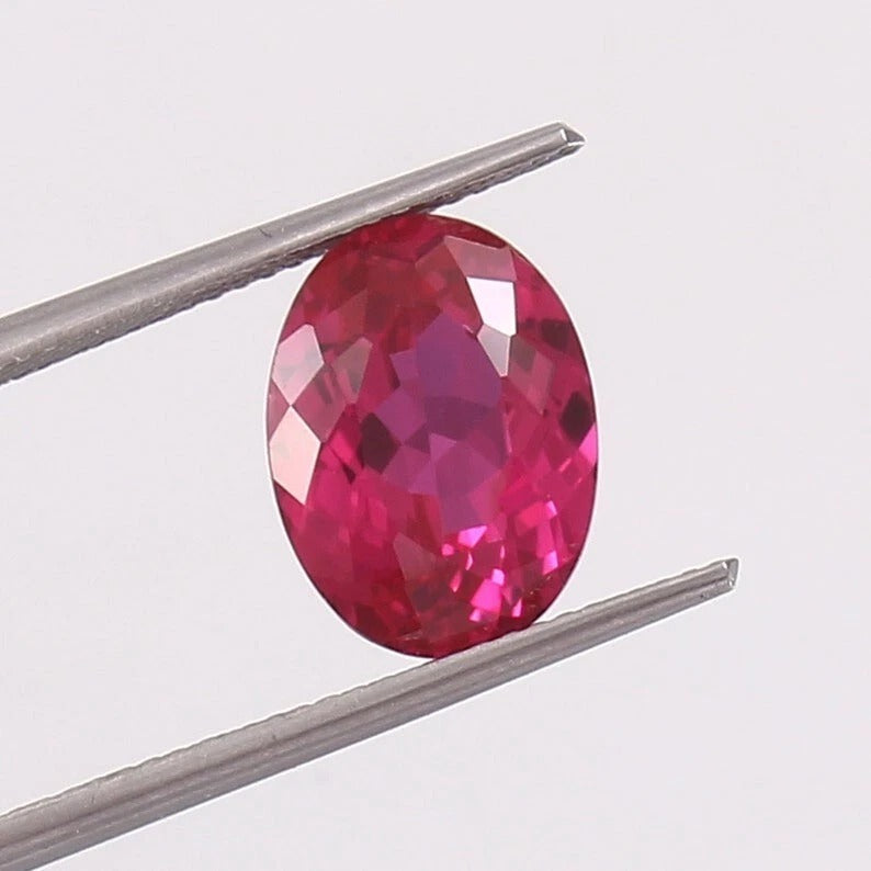 Faceted Ceylon Pink Sapphire gemstone held between tweezers on a light gray background