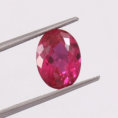 Faceted Ceylon Pink Sapphire gemstone held between tweezers on a light gray background