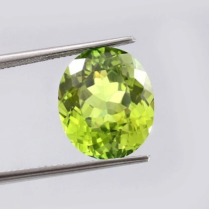 Green Peridot gemstone held between tweezers against a light gray background