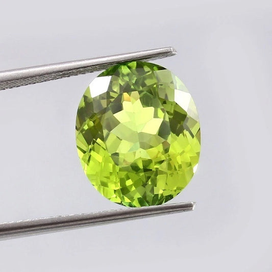 Green Peridot gemstone held between tweezers against a light gray background
