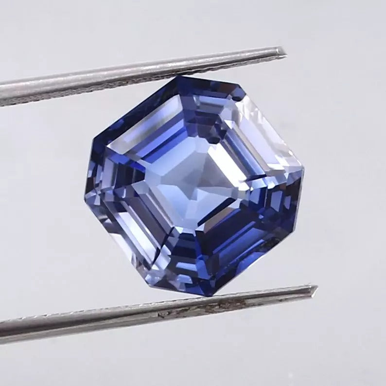Ceylon Blue Sapphire gemstone held between tweezers on a light gray background