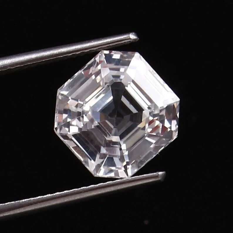 Asscher-cut White Sapphire held between tweezers against a black background