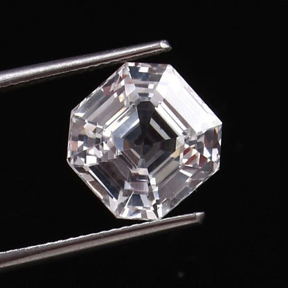 Asscher-cut White Sapphire held between tweezers against a black background