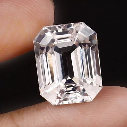 Emerald cut White Sapphire held between fingers against a dark background