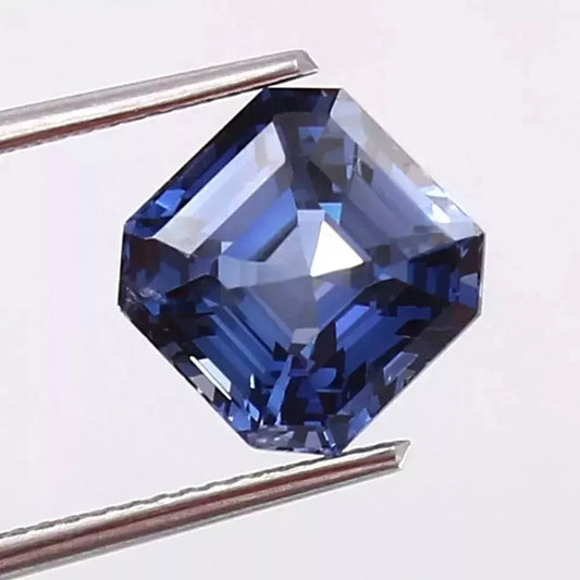 Blue sapphire gemstone held by tweezers on a white background