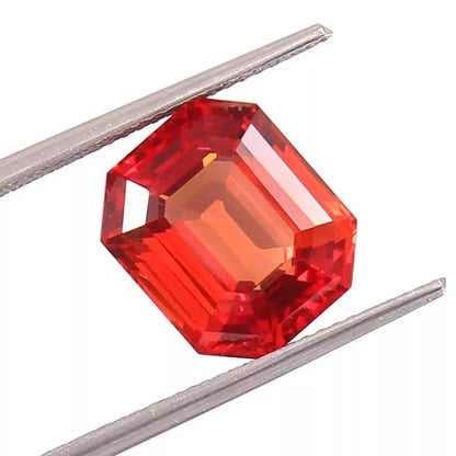 Fanta Orange Sapphire gemstone between two metal prongs on a white background