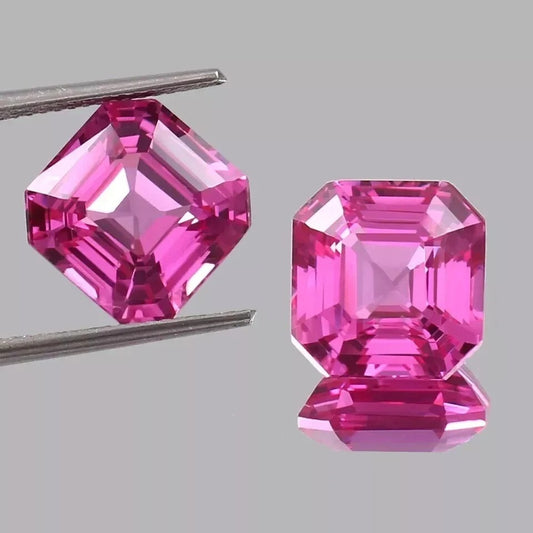 pair Ceylon Pink Sapphire gemstones held by tweezers on a gray background