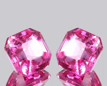 pair Ceylon Pink Sapphire gemstones on a reflective surface with a light gray background