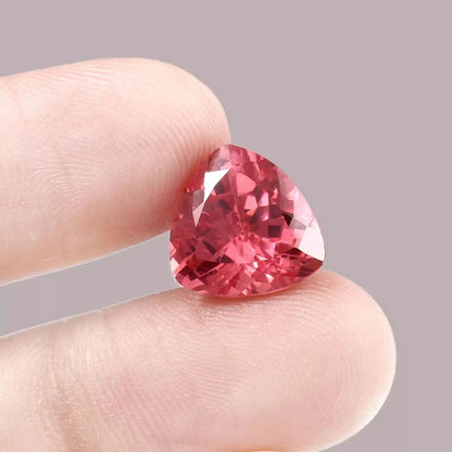 Trillion-shaped Padparadscha Sapphire gemstone held between fingers against a neutral background