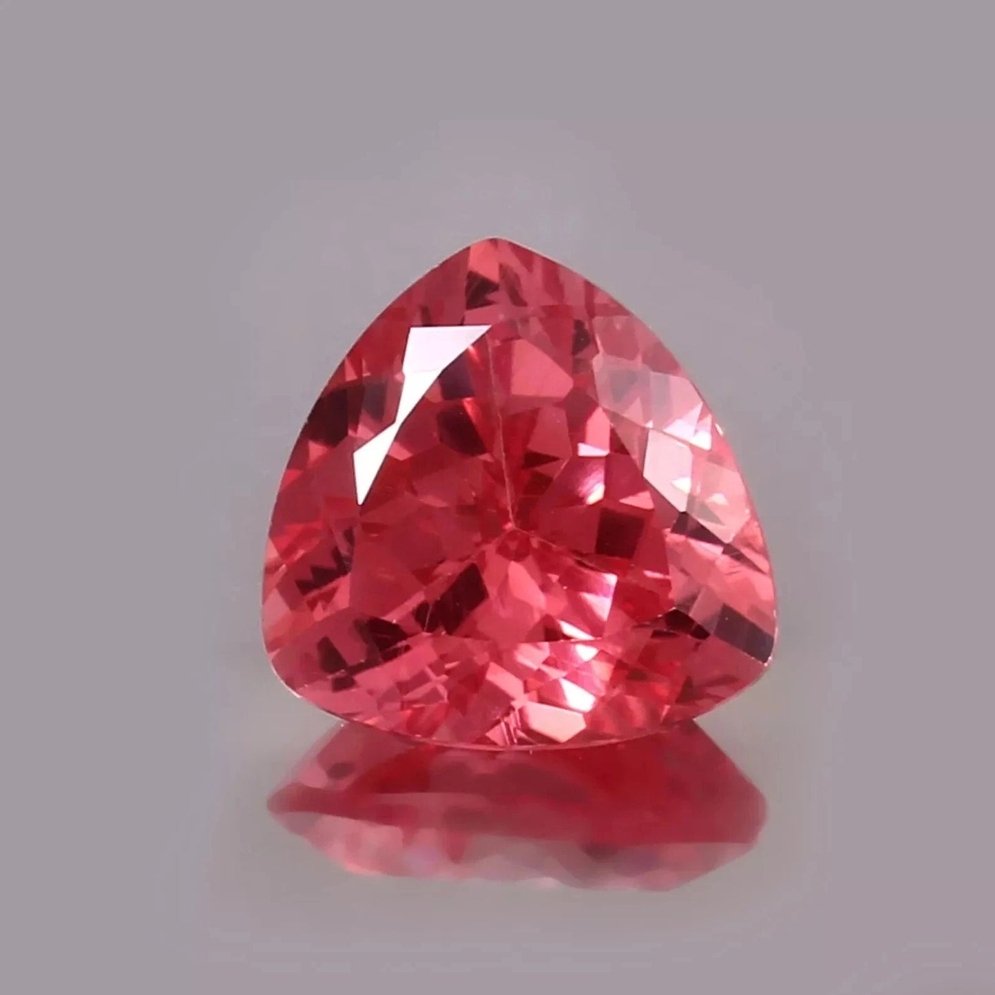 Trillion-shaped Padparadscha Sapphire gemstone on a gray background