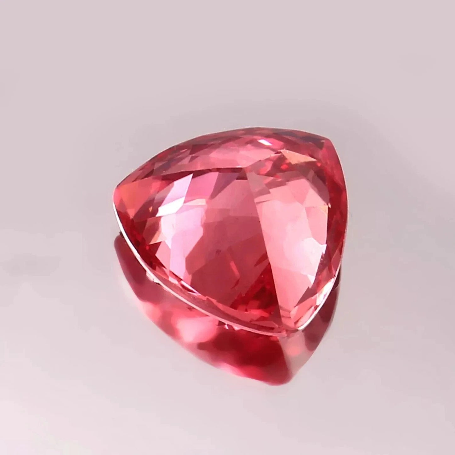 Trillion-shaped Padparadscha Sapphire gemstone on a light gray background
